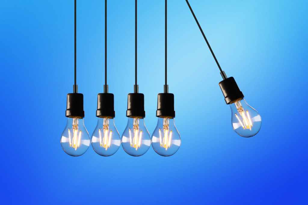 Image of five shining light bulbs hanging in a row. Four are touching and one is swinging out to the right.